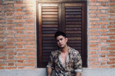 Portrait of young man sitting against brick wall