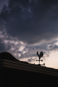 Low angle view of weather vane against cloudy sky