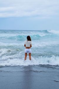 Rear view of woman standing at beach against sky