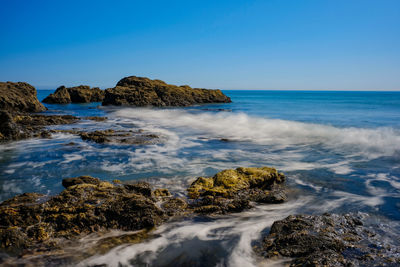 Scenic view of rocks in sea against clear blue sky