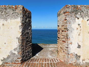 Stone wall by sea against clear blue sky