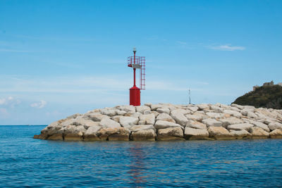 Lighthouse on rock by sea against blue sky