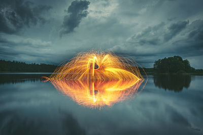 Woman with wire wool over lake against cloudy sky