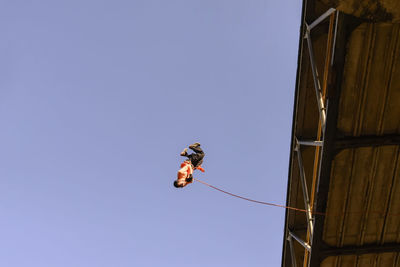 Low angle view of man rappelling against clear sky