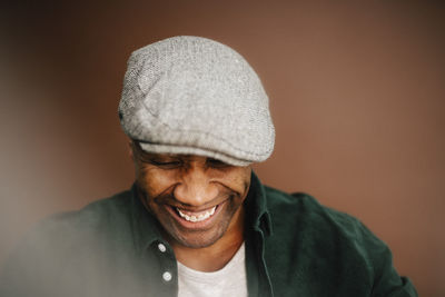 Happy mature man wearing beret looking down over brown background