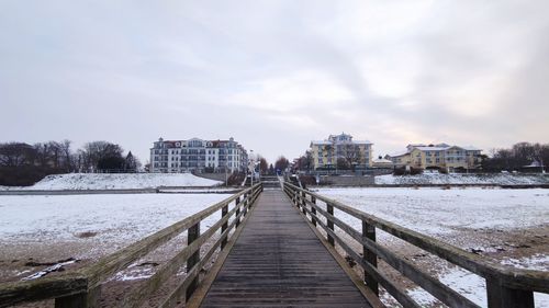 Pier amidst buildings in city against sky during winter