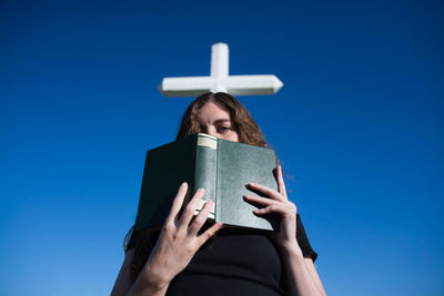 Low angle view of woman holding bible against cross