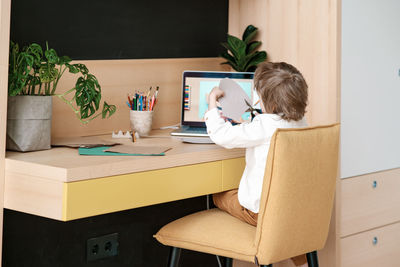 Rear view of man using phone while sitting on table