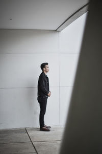 Side view of young man looking away against wall