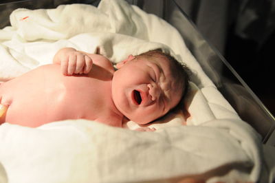 High angle view of naked newborn baby boy lying on bed at hospital