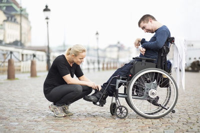 Female caretaker putting on disabled man's shoes on street