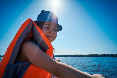 Portrait of girl wearing life jacket while sitting in boat against sky on sunny day