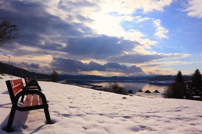 Empty chairs and tables on snow covered land against sky