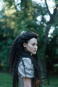 Portrait of young woman looking at tree in forest