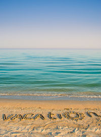 Vacation text on sea shore against clear sky