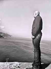 Side view of man standing on pier against sky at beach