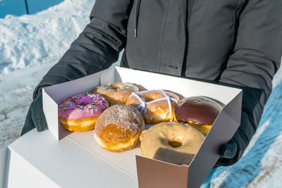 Midsection of woman holding fresh donuts in cardboard box during winter