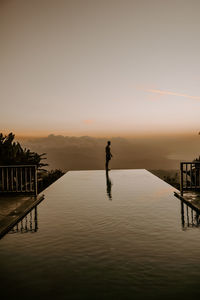 Silhouette man standing by pool against sky during sunset