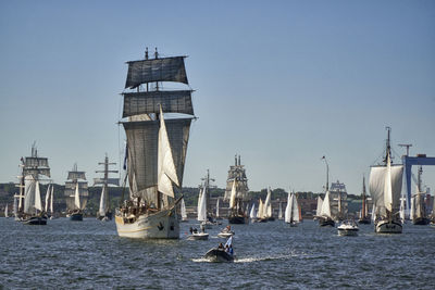 Sailboats in sea by buildings against clear sky