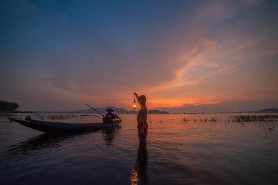 Silhouette man standing in sea against sky during sunset