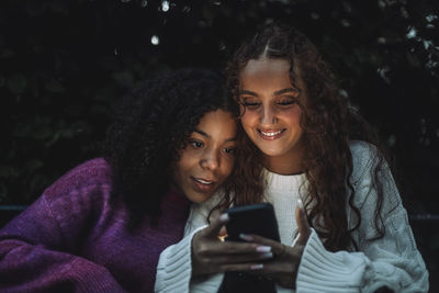 Smiling girl sharing smart phone with curious female friend
