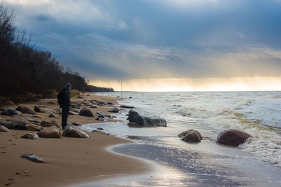 Person standing at sea shore against cloudy sky