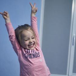 Portrait of young woman with arms raised standing against wall