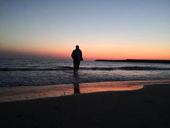 Silhouette man standing on beach against sky during sunset