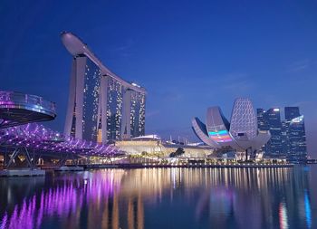 Illuminated city buildings by river against sky