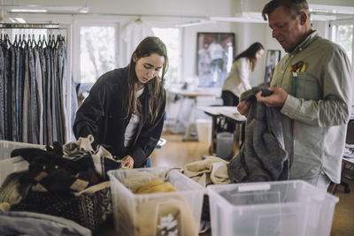 Female fashion designer with male colleague sorting recycled clothes while working at workshop