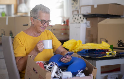 Smiling woman holding coffee cup using phone at home