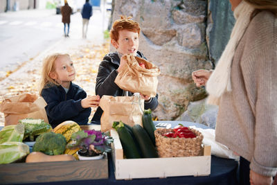 Male and female sibling buying vegetables from female market vendor