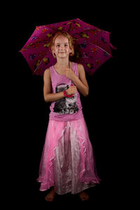 Portrait of smiling girl in pink dress holding umbrella against black background