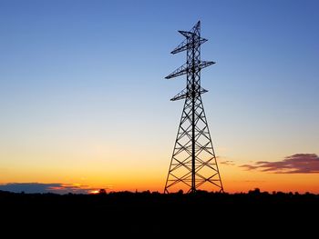 Low angle view of silhouette electricity pylon on field against sky during sunset