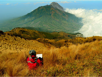 High angle view of teenage boy sitting on grassy mountain