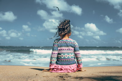 Rear view of woman on beach against sky