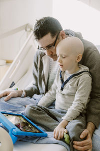 Father recovering from surgery watches tablet with son in hospital