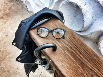 High angle view of eyeglasses with leather jacket and umbrella on wooden bench
