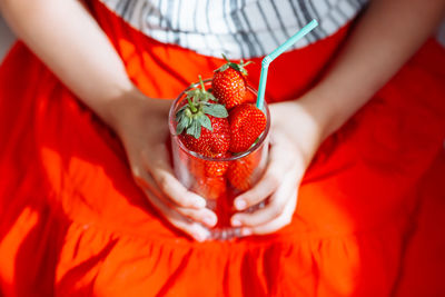 The hands of a girl in a red skirt hold a glass with juicy strawberries.