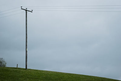 Low angle view of electricity pylon on field against sky