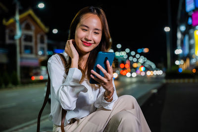 Portrait of young woman using mobile phone at night
