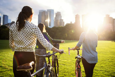 Rear view friends walking with bicycles on field in central park