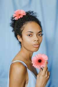 Woman in blue dress holding fresh gerbera daisy by curtain