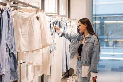 Young woman stands in a fashion store, carefully choosing clothing items to buy. she browses through