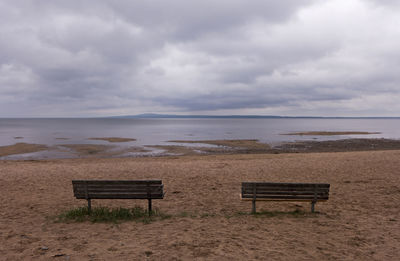 Empty bench on beach against sky