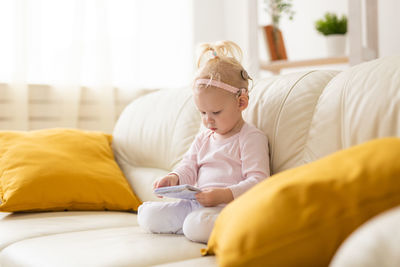 Girl holding book while sitting on sofa