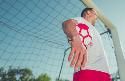 Low angle view of man with ball standing by goal post