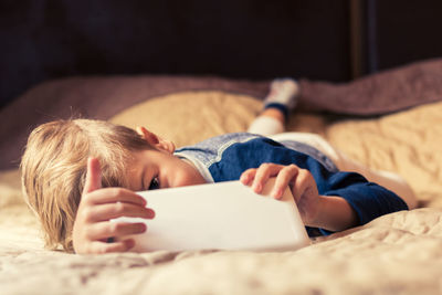 Boy using digital tablet while lying on bed at home