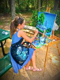 Full length of smiling woman painting while sitting on bench