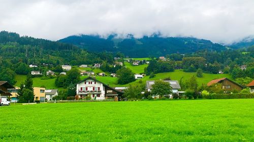 Houses on field by buildings against sky